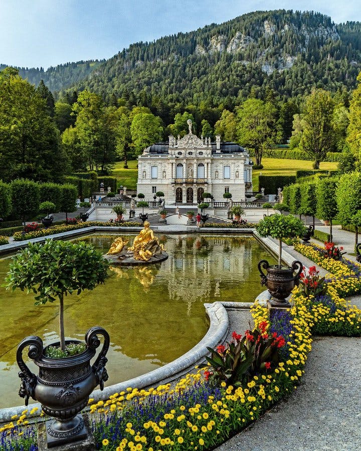 <p>Schloss Linderhof is a palace in southwest Bavaria, Germany, near the village of Ettal. It is the smallest and the only completed palace of King Ludwig II of Bavaria, who lived there from 1876 until his death in 1886. Schloss Linderhof was inspired by the palace of Versailles in France, especially the style of Louis XIV, the Sun King. However, it also reflects Ludwig’s personal taste and imagination, as well as the landscape and culture of Bavaria. </p><p><br></p><p><u>Here is some more information about Schloss Linderhof:</u></p><p><br></p><p>The palace was built on the site of a former hunting lodge that belonged to Ludwig’s father, King Maximilian II. Ludwig enlarged and transformed the lodge into a rococo palace with stone façades and lavish interiors. He also added three new rooms and a staircase to the U-shaped complex. The palace cost about 8.5 million marks to construct.</p><p><br></p><p>The palace has only four rooms that serve a real function: the bedroom, the dining room, the audience room, and the living room. The bedroom is the largest and most important room, as it symbolizes the absolute monarchy of Louis XIV and Ludwig’s self-image as a <em>Night-King</em>. The dining room features a mechanical table that could be lowered to the kitchen below and raised again with the food, allowing Ludwig to dine alone without servants. The audience room and the living room are decorated with portraits of French kings and courtiers, as well as scenes from French history and mythology.</p><p><br></p><p>The palace is surrounded by a large park that contains several buildings and attractions, such as the Venus Grotto, a artificial cave with a lake and a waterfall, where Ludwig could enjoy Wagner’s operas in a boat; the Moorish Kiosk, a pavilion with an oriental design and a peacock throne; the Moroccan House, a replica of a North African dwelling with exotic furniture and weapons; the Hunding’s Hut, a rustic cottage from Wagner’s opera <em>The Valkyrie</em>; and the Hermitage of Gurnemanz, a neo-Gothic chapel from Wagner’s opera <em>Parsifal</em>.</p><p><br></p><p>Schloss Linderhof is one of the four palaces that Ludwig II built or planned to build during his reign. The others are Neuschwanstein, Herrenchiemsee, and the unfinished Falkenstein. These palaces are considered as Ludwig’s <em>built dreams</em>, as they express his artistic vision and his longing for a different world. In 2019, these palaces were officially nominated for the UNESCO World Heritage List, as they represent a unique cultural phenomenon and a testimony to Ludwig’s legacy.</p><p><br></p>
